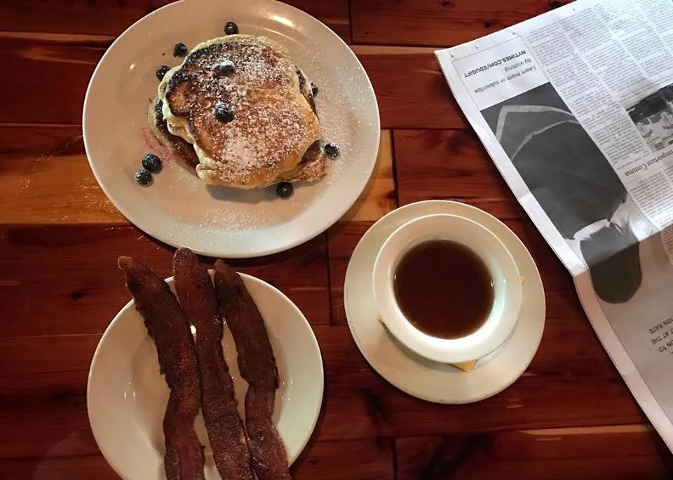 Pancakes with blueberries, a side of bacon and a cup of coffee on a wooden table