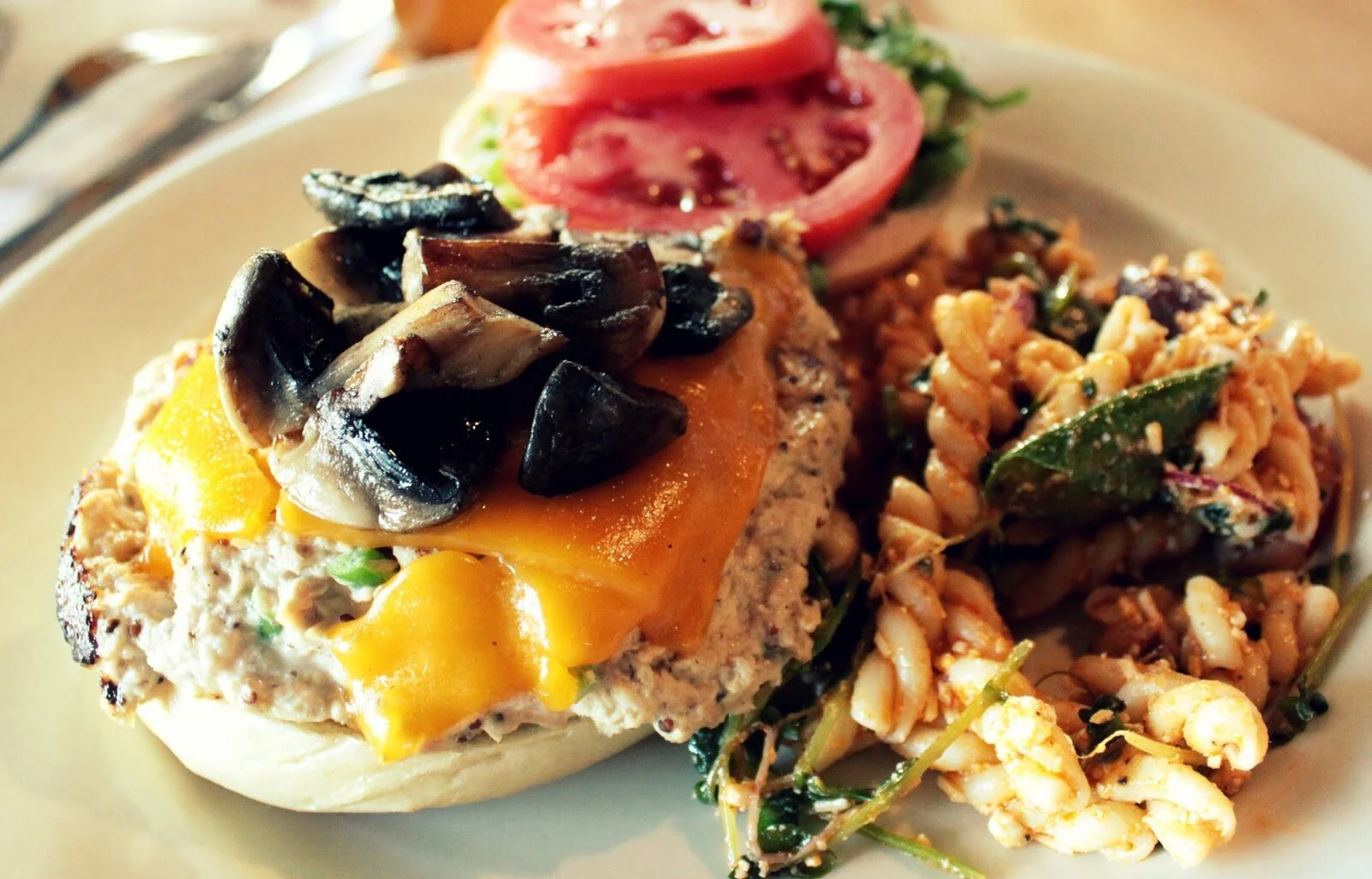 An open burger with melted cheese, mushrooms and tomato, piled with shoestring potatoes