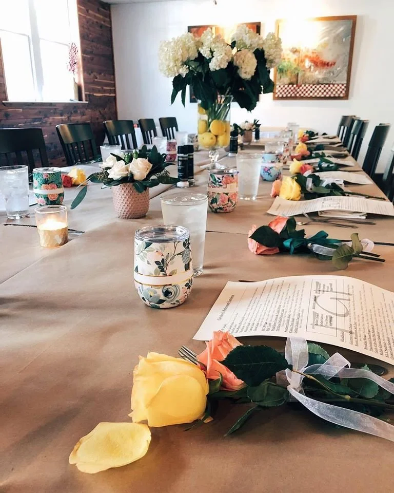 A long table laid end to end for a party, with flowers, candles and printed menus