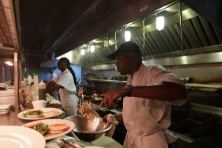 A cook plating a dish on the line, under the kitchen hood