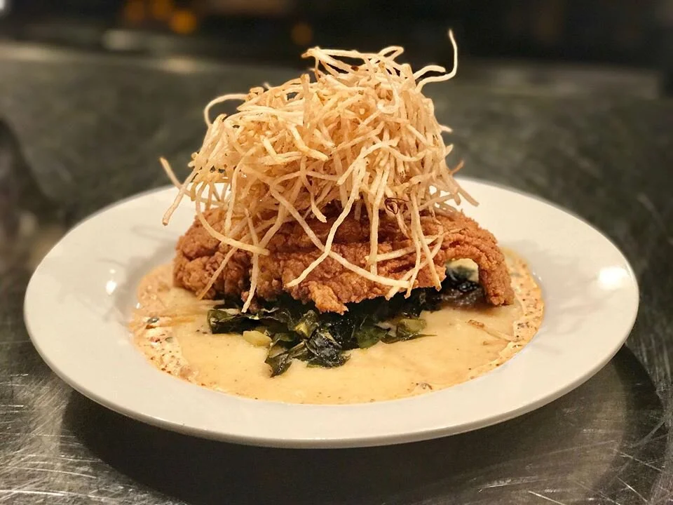 A pan fried cutlet over greens and grits, crowned with a nest of shoestring potatoes