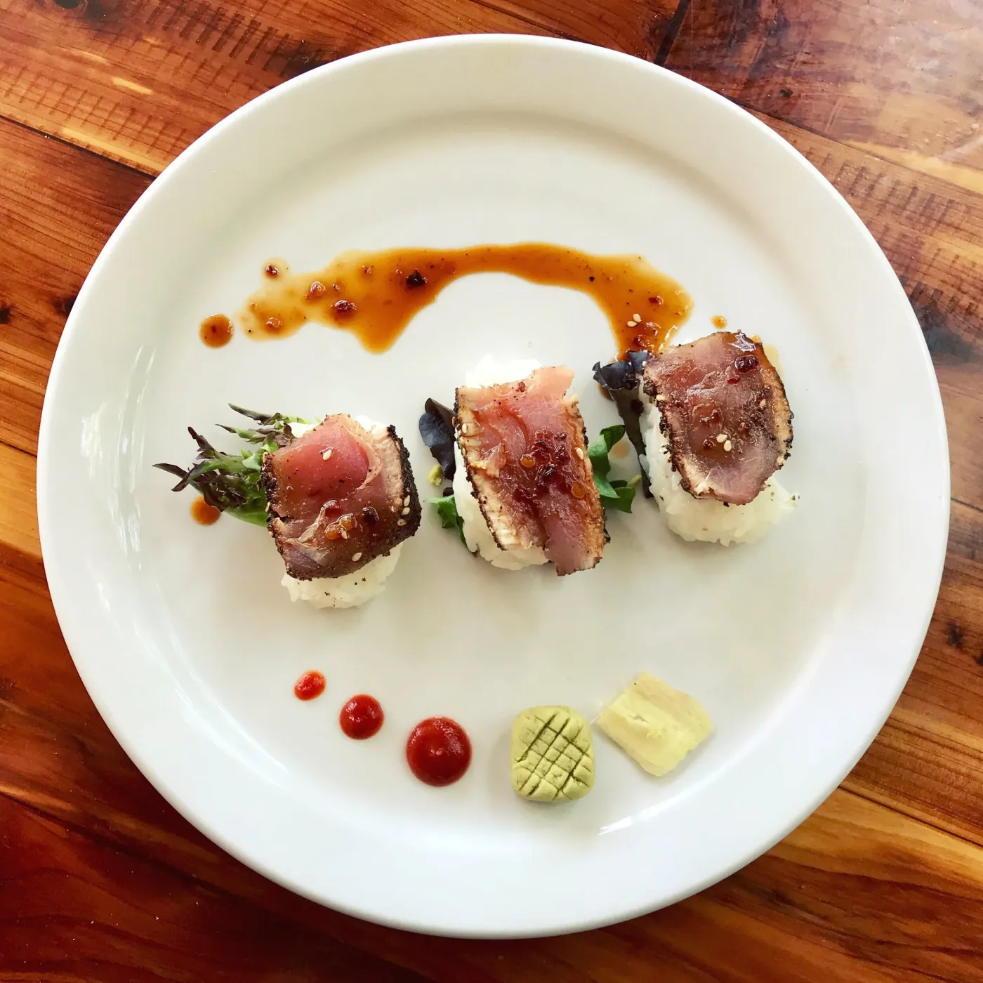 Three seared tuna medallions on rounds of rice, dotted with red and yellow sauce